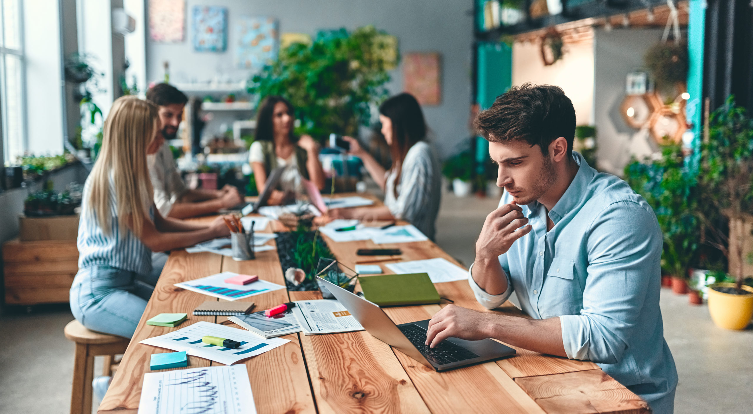 tendance espace de travail 2022 : Personnes qui travaillent autour d'une table en bois dans un espace végétalisé