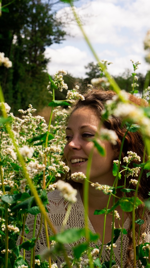 Une femme (Floriane) est dans un champs de fleur et elle sourit