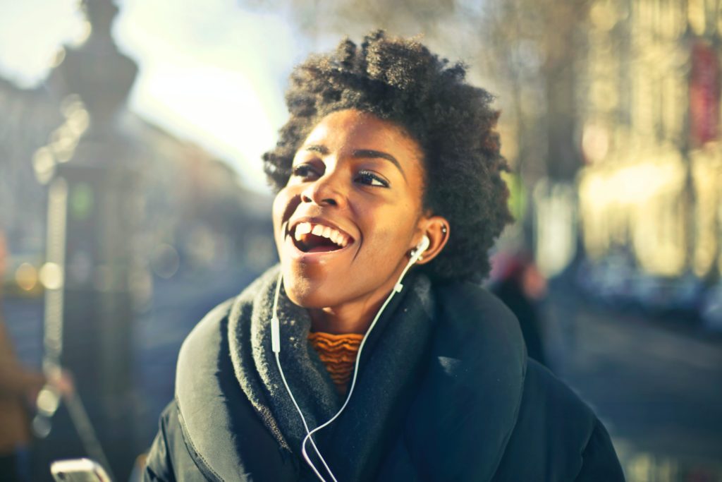 Femme dans la rue qui sourit avec des écouteurs dans les oreilles