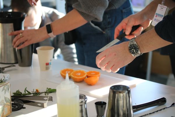 une table avec des ustensiles pour préparer un cocktail et une personne couper des oranges
