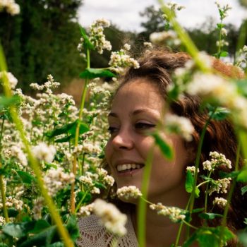 Une femme (Floriane) est dans un champs de fleur et elle sourit